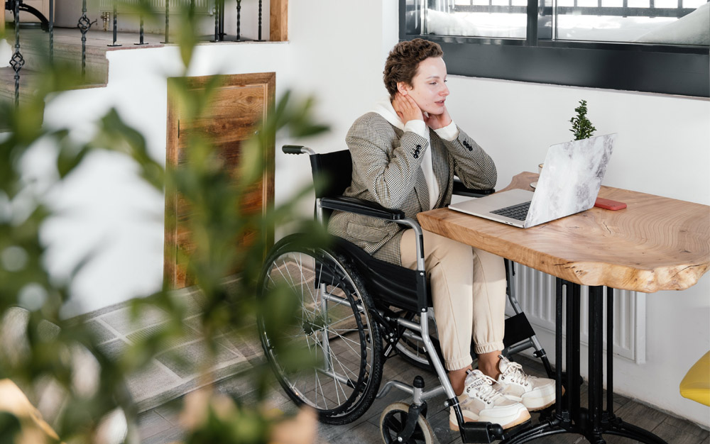 Woman in wheelchair using laptop on desk